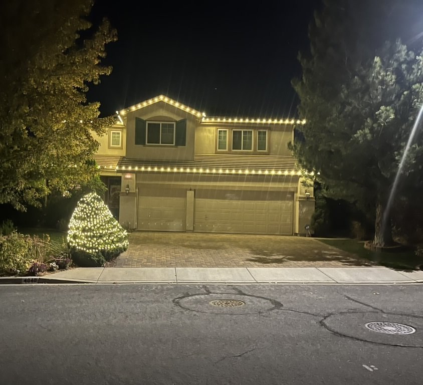 Two-story home with warm white roofline and lit evergreen